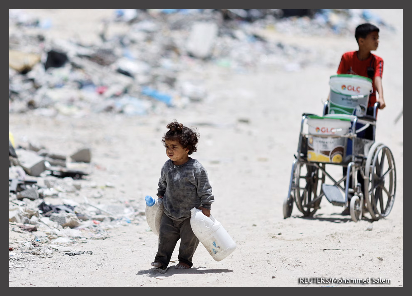 Una niña palestina carga latas para recoger agua mientras pasa junto a casas que fueron destruidas en un ataque israelí, en medio del actual conflicto entre Israel y Hamás, en Khan Younis, en el sur de la Franja de Gaza. REUTERS/Mohammed Salem